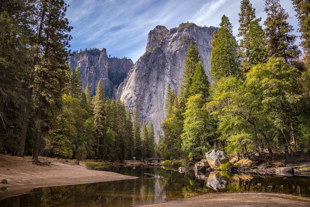 Scenic photo of large rock in distance and trees with placid stream in foreground